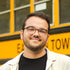 Jeune homme portant des lunettes au cheveux brun devant un autobus scolaire jaune