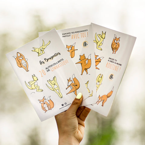 Main tenant trois feuilles d’autocollants Les Bougeottes en nature, mascottes renard et kangourou en mouvements de gymnastique.
