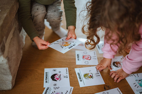 Cartes d'apprentissage émotions (joie, colère, dégoût) au sol d'une garderie avec des enfants en petite enfance qui jouent et bougent avec les cartes. 
