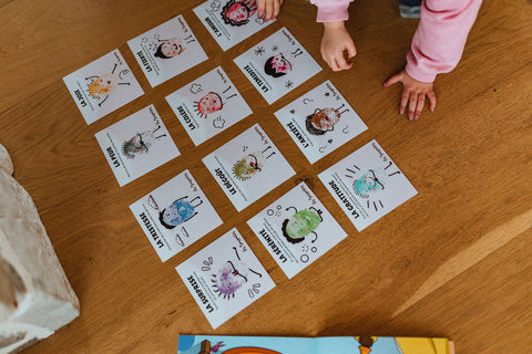 Cartes d'apprentissage émotions (joie, colère, dégoût, peur, tristesse) au sol d'une garderie avec des enfants en petite enfance qui jouent et bougent avec les cartes. 