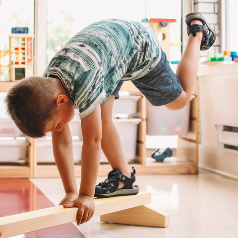 Poutre de gymnastique en bois dans une garderie avec un enfant réalisant le mouvement de l’aiguille.
